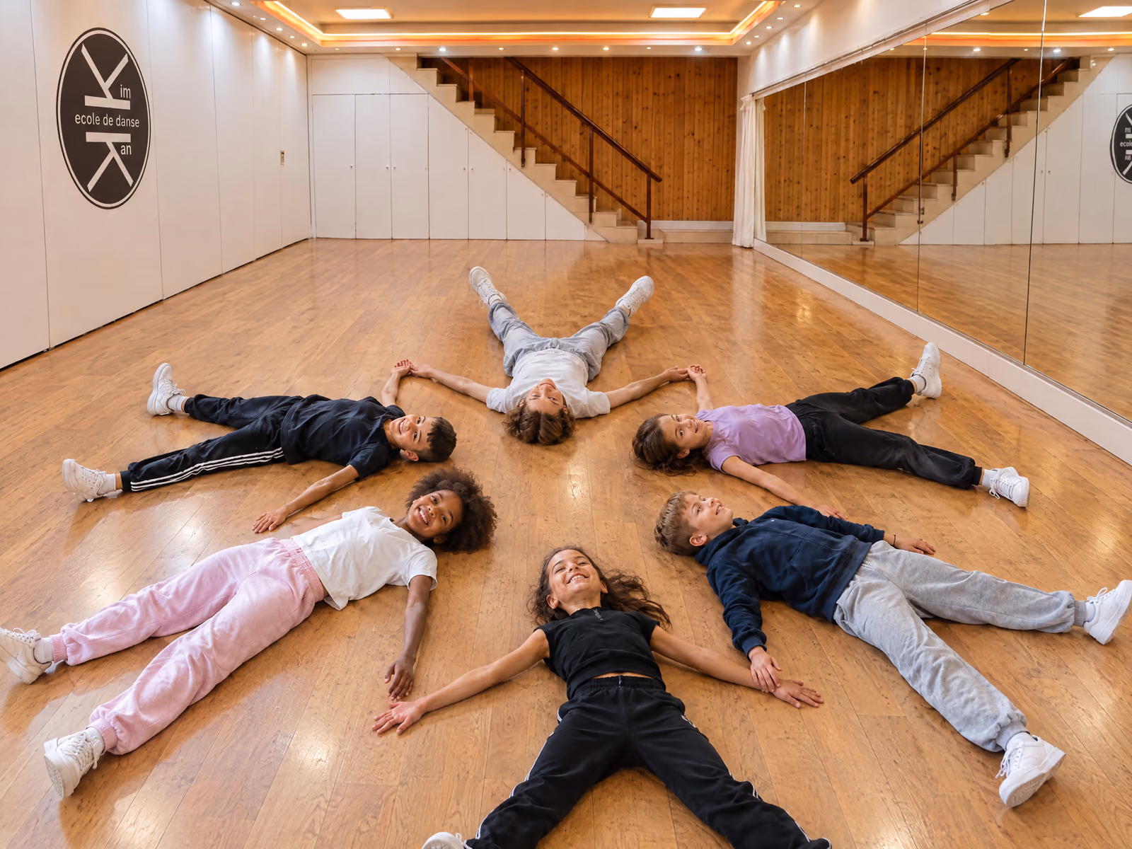 Initiation 6-7 ans : des enfants allongés en étoile sur le parquet de la salle 3 de Gambetta, la tête au centre.