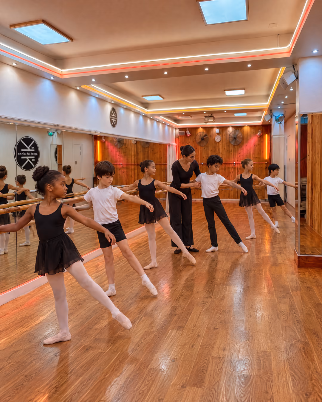 Classique enfants : filles et garçons à la barre en tendu, en chaussons, la professeure au milieu d’eux, dans la salle 2 de Gambetta.
