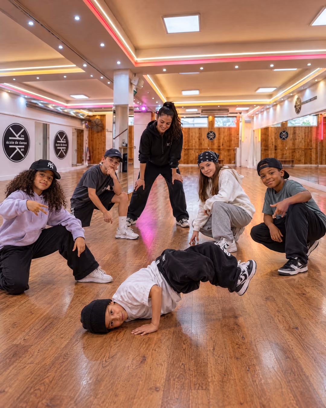 Hip-hop enfants : des enfants en sweat, casquette et baskets tiennent un freeze, un garçon en appui au sol, dans la grande salle de Gambetta.