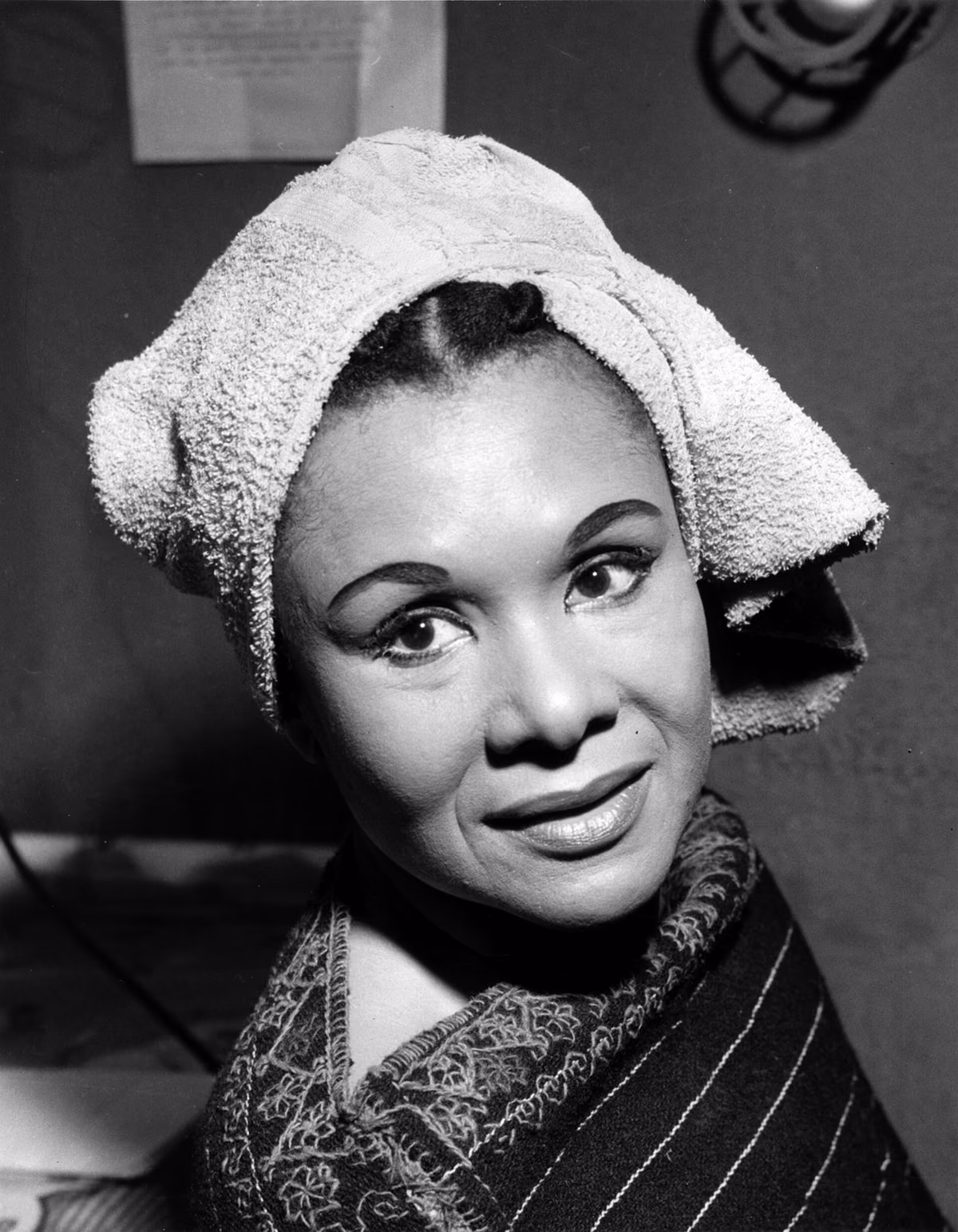 Katherine Dunham en 1956, souriante, une serviette nouée sur la tête, en coulisses.