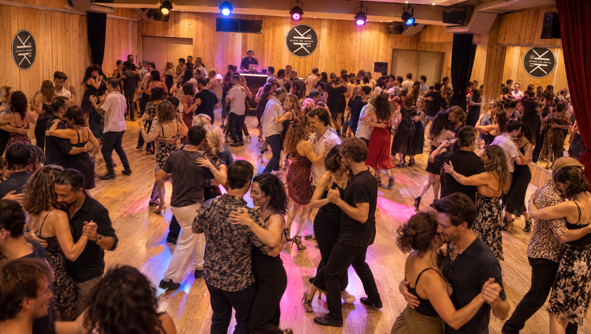 Un soir de bal au Studio des Rigoles vu d’en haut : des couples sur le parquet sous les projecteurs colorés, le DJ au fond.
