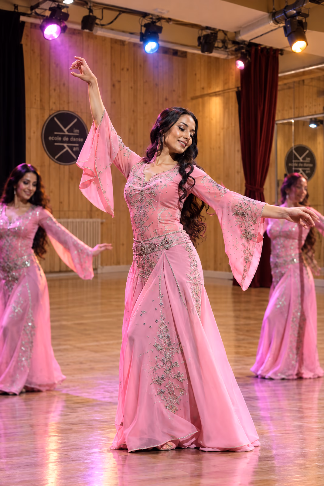 Danse orientale : des danseuses en longues robes roses brodées, bras en courbe, sous les projecteurs colorés du Studio des Rigoles.